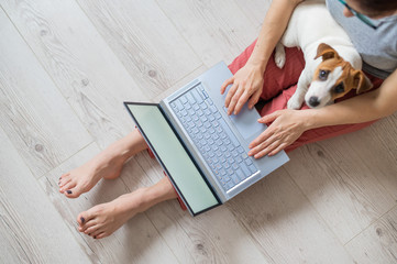 Faceless woman working from home. Unrecognizable girl sitting on the floor with a puppy of Jack...