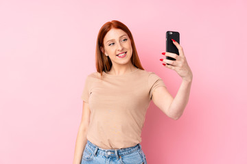 Young redhead woman over isolated pink background taking a selfie with the mobile