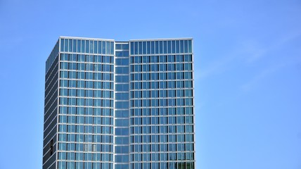 Blue curtain wall made of toned glass and steel constructions under blue sky. A fragment of a building.