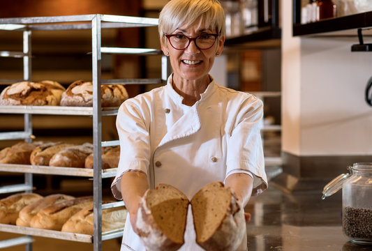 Portrait of senior female baker holding bread in her hands at bakery.