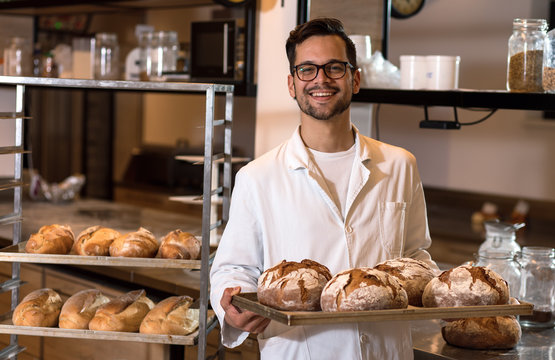 Portrait of young male baker holding bread in his hands at bakery.