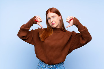 Young redhead woman over isolated blue background showing thumb down