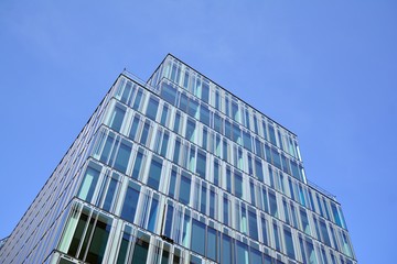Blue curtain wall made of toned glass and steel constructions under blue sky. A fragment of a building.