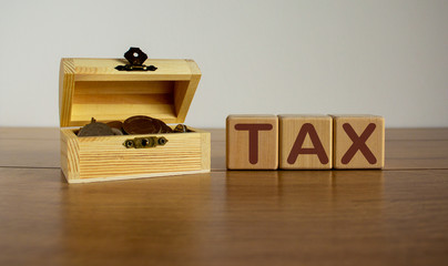 Concept word tax on cubes on a beautiful wooden table, small chest with coins.