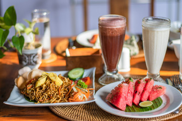 Balinese breakfast served on a table with noodles, watermelon and colourful smoothie