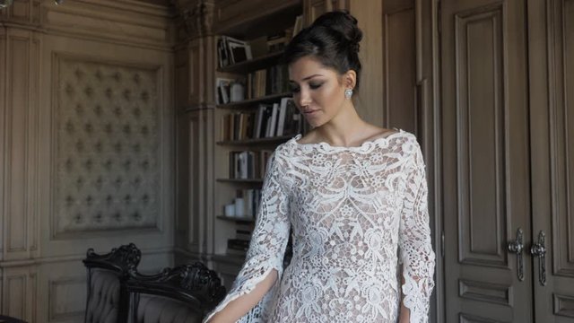 attractive lady in white lacy tight wedding dress walks past decorated chairs before celebration in design studio slow motion