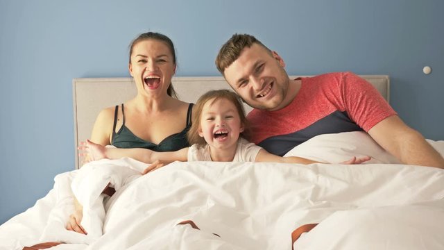 Fun family morning. Dad, mom and little daughter are playing in bed. All together are hiding under the covers.