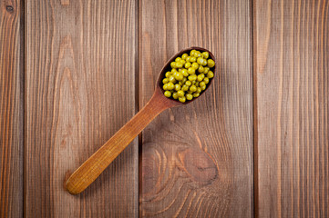 Canned green peas in a wooden spoon lying on a wooden surface of the table.