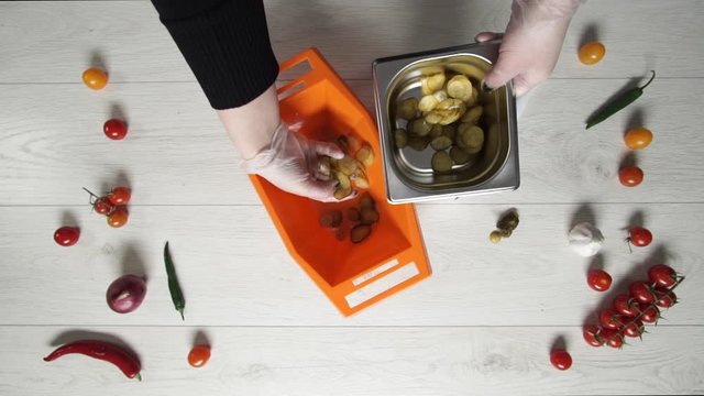 Chief takes slice of pickle cucumbers from plastic bowl and puts them to metal container