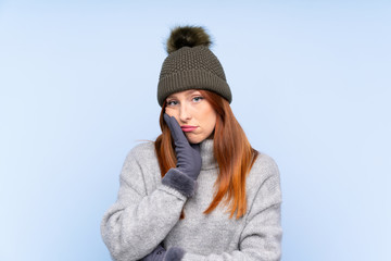 Young redhead Russian woman with winter hat over isolated blue background unhappy and frustrated