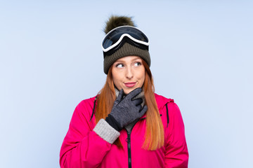 Skier redhead woman with snowboarding glasses over isolated blue wall thinking an idea