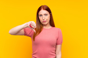 Young redhead woman over isolated yellow background showing thumb down sign