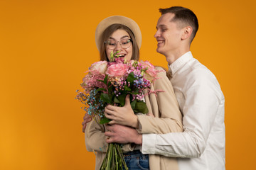 Excited couple with flowers embracing isolated on yellow background
