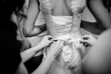 Friends lace corset on the bride's dress. Bridesmaids dress the bride with a slender waist in a...