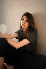 Portrait of a girl with brown hair sitting at home on the bed near the wall