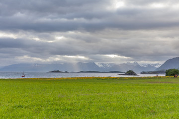 Lone ship in the water of the Norwegian fjords. cloudy sky, green grass. Lofoten.