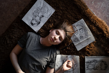 portrait of a girl lying on a sofa around her drawings are scattered, view from above