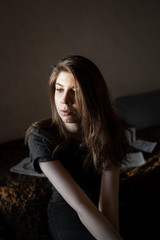 portrait of a girl with brown hair, sitting at home on the bed, look out the window