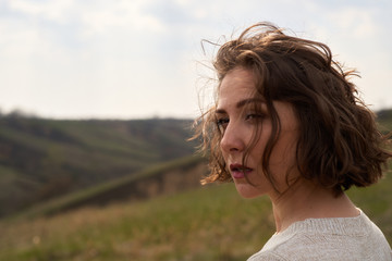 Portrait of beautiful girl on nature view background with hills and sky. Young woman is looking...