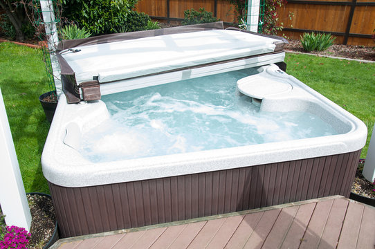 Hot Tub In Back Yard With Water Bubbling And The Lid Half Off, Ready To Be Enjoyed In The Outdoors.