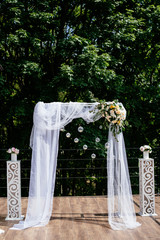 Outdoor photographic area is a stylish wedding decoration. Wedding arch, decorated with flowers, mini florals. Beautiful wedding ceremony outdoors place for celebration.