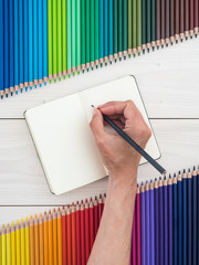caucasian female hand writing on notebook, colorful pencils background