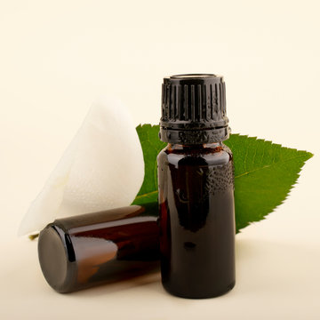 Essential Aromatherapy Oils. Photo mockup for your product. Glass dark bottle of aroma oil with a white rose bud and a green leaf.