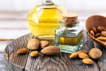 Concept of organic vegetable oils for cooking and cosmetology. Almond nuts to illustrate ingredients. Rustic wooden background, natural oil in glass bottles. Close up, macro