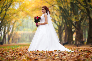 Obraz na płótnie Canvas Young bride in wedding dress walking in a park. White luxury gown fashion for woman. The bride walks in the park.