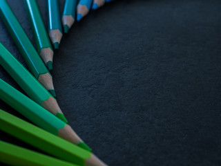 Set of colored pencils arranged in a wheel on slate background