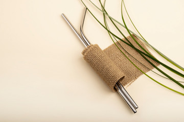 Reusable Metal Straws with Portable Case - Stainless Steel, Eco-Friendly Drinking Straw Set with  Cleaning Brushes. Metal straw on a pastel background with green grass and brown burlap cloth.