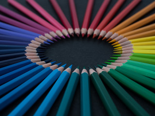 Set of colored pencils arranged in a wheel on slate background