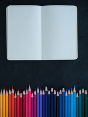 row of colored pencils and notebook on slate background