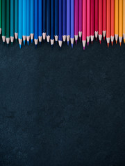 Set of colored pencils arranged in a row on slate background