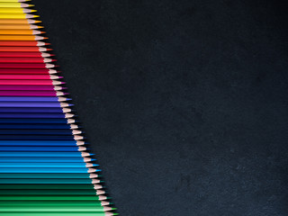 Set of colored pencils arranged in a row on slate background