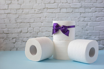 Four rolls of toilet paper on white brick wall background. Toilet roll with purple bow