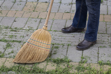 Women cleaning cut grass from pavement using classic broom made from natural materials