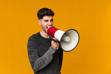 Young man over isolated background shouting through a megaphone
