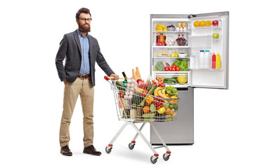Bearded man with a shopping cart and an open fridge full of food products © Ljupco Smokovski