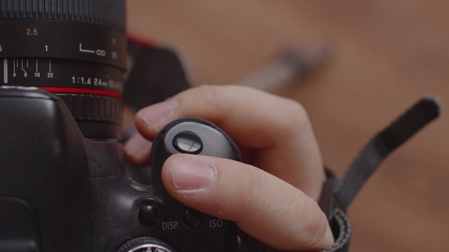 Close - up from above on the photographer's hand pressing the camera shutter and adjusting the shutter speed. The man's finger clicks on the photo button and changes the camera's indicators
