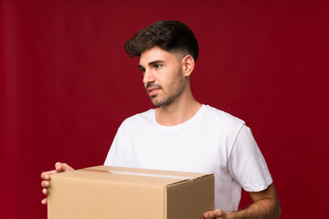 Young man over isolated background holding a box to move it to another site