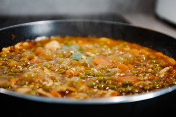 Side view of a pan cooking a rice and chicken paella in Spain during confinement