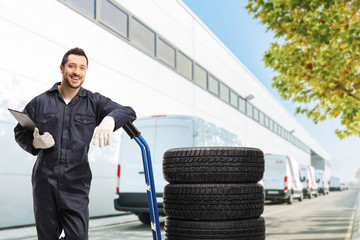 Fototapeta na wymiar Male worker in a uniform standing with tires on a hand truck outside a warehouse