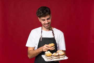 Young man over isolated background holding mini cakes and surprised