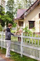 Middle aged man talking to his female neighbor over wooden fence on way home in countryside