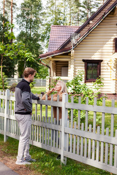 Middle Aged Man Talking To His Female Neighbor Over Wooden Fence On Way Home In Countryside