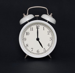 Old-style alarm clock, black and white, it's five o'clock.