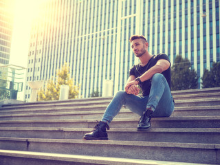 One handsome young man in urban setting in European city, wearing jeans and black t-shirt