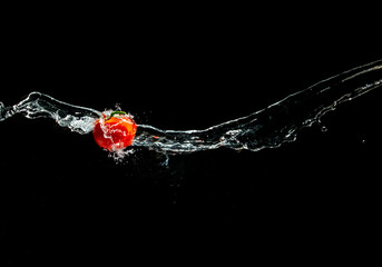 Fresh ripe red tomato with green leave flying in wave of water in the air isolated on black background. Concept of food levitation