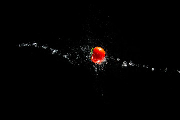 A fresh ripe red tomato with a green leaf flies in the air in water drops isolated on a black background. Concept of food levitation